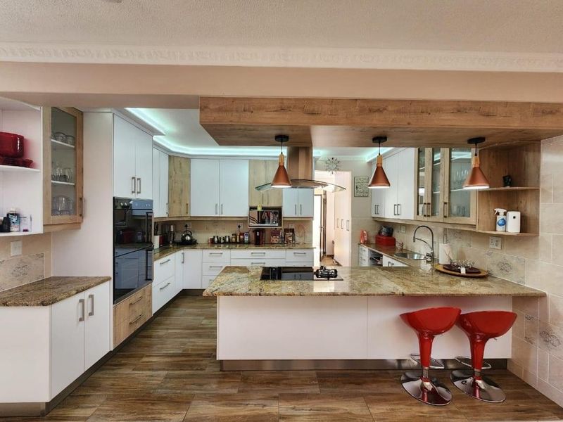 Modern kitchen featuring granite countertops, built-in oven, hob, extractor fan, and ample cabinetry with integrated lighting and wood-look tiled flooring.