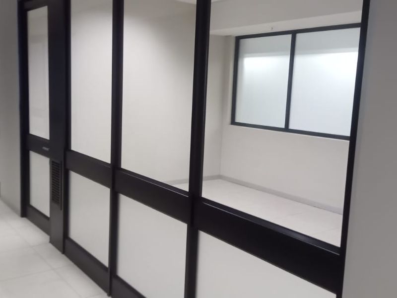 A bright, modern office hallway featuring glass partition walls, aluminum framing, and clean tiled flooring, providing a professional and open workspace environment.