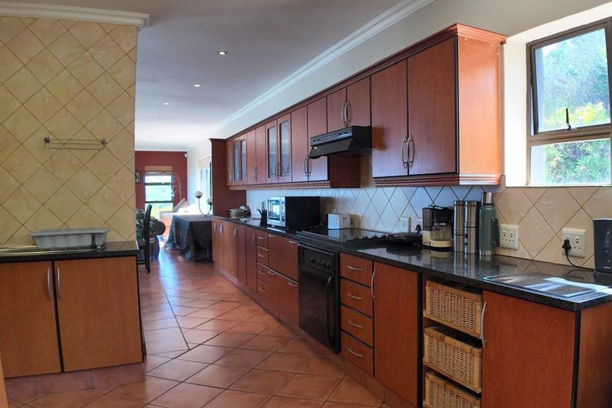 Spacious kitchen featuring wooden cabinetry, dark granite countertops, tiled flooring, and integrated appliances, flowing into an open-plan living area.
