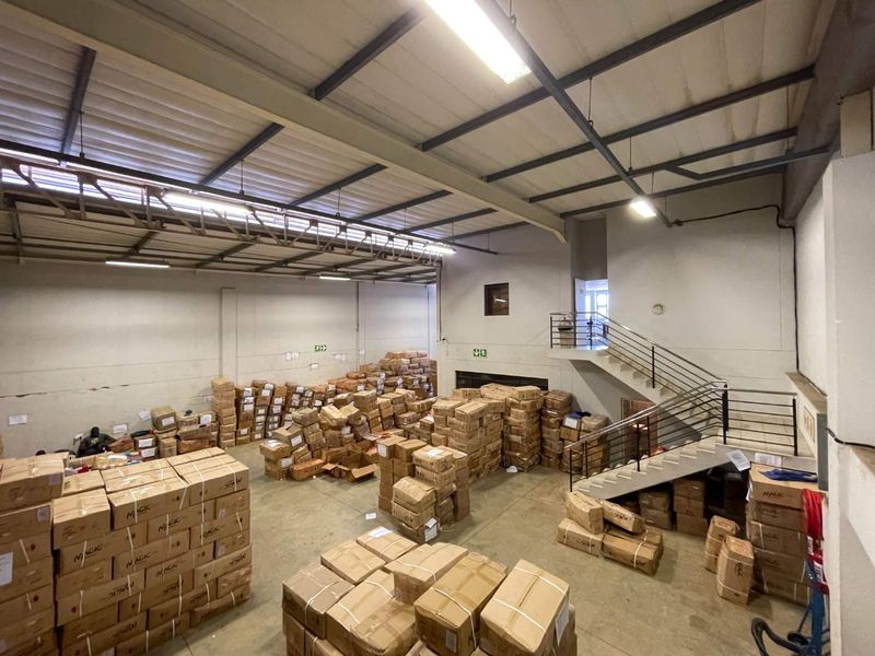 Spacious industrial utility or warehouse area featuring high ceilings with exposed steel trusses, concrete flooring, and an internal staircase leading to an upper level.