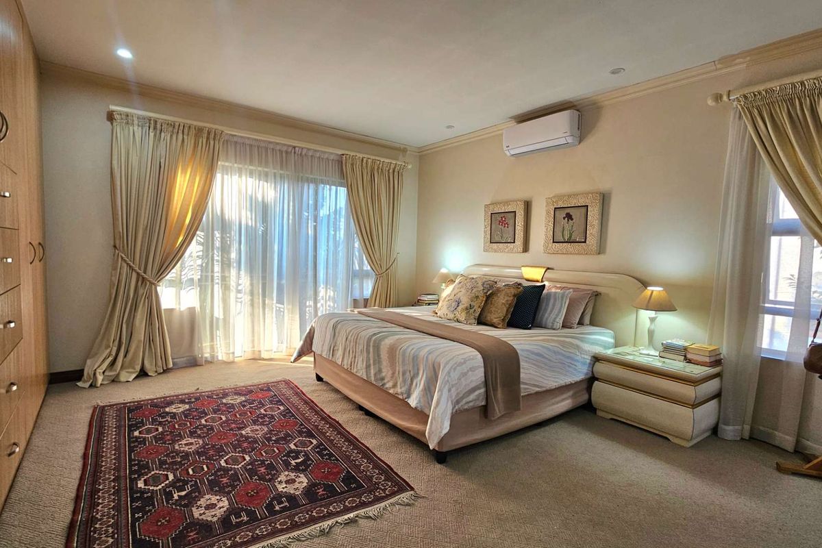 Spacious bedroom featuring built-in wooden cabinetry, wall-mounted air conditioning unit, and large windows with curtains allowing for ample natural light.