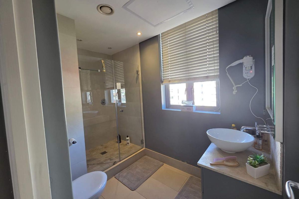 Modern bathroom featuring a glass-enclosed shower, vessel sink vanity, and neutral tile finishes with recessed lighting.