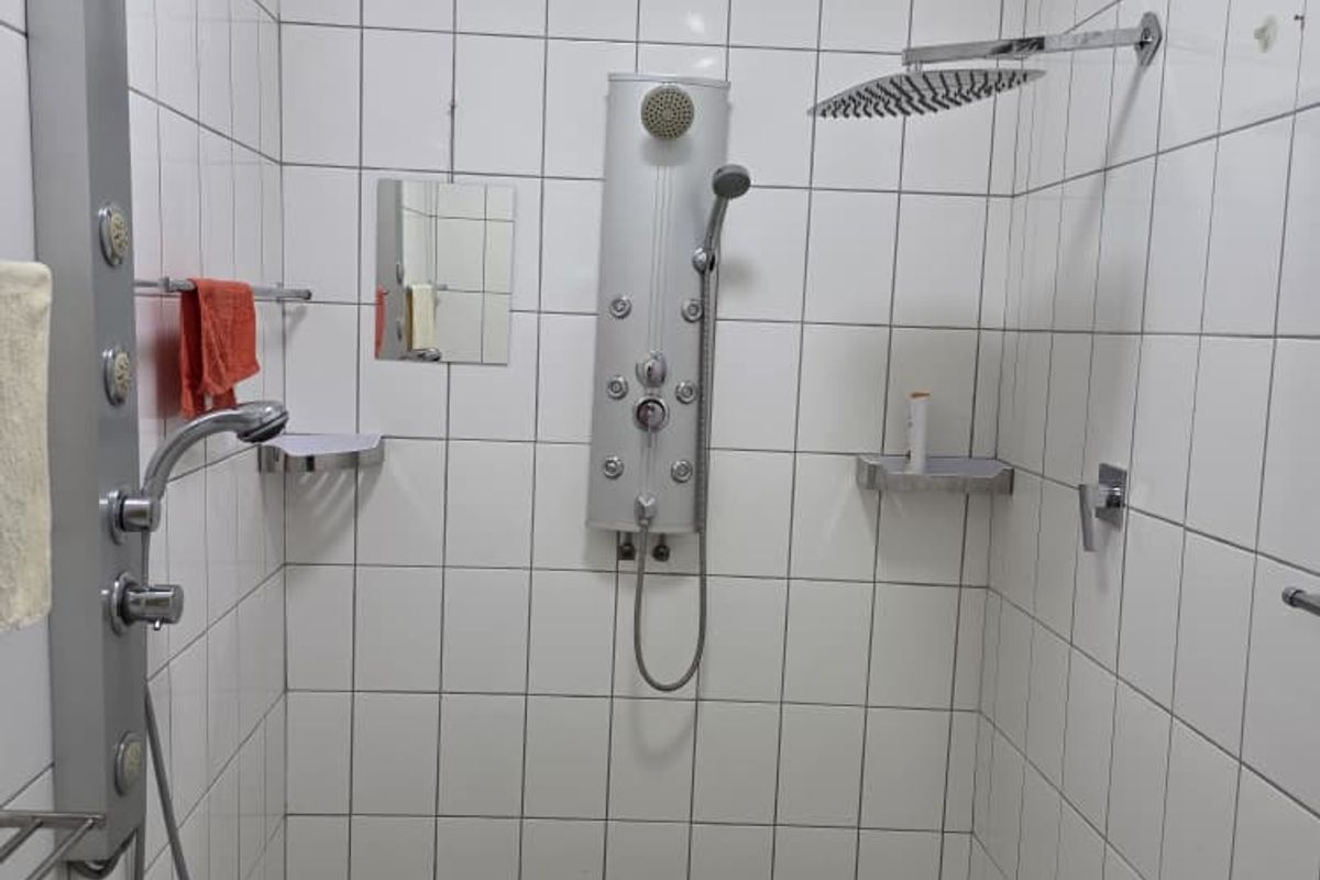 A walk-in shower enclosure featuring white wall tiling, mosaic floor tiles, and multiple shower panel systems.