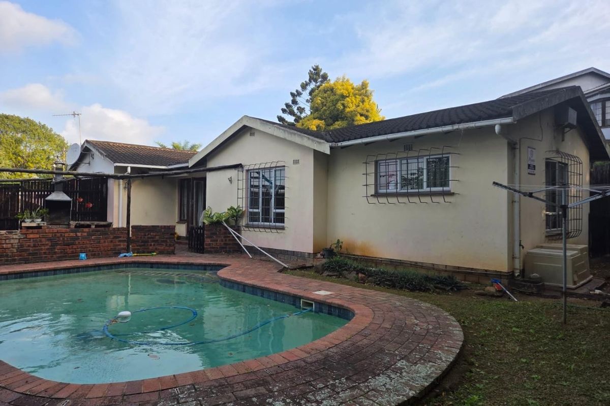 Rear view of the property featuring a swimming pool with brick surround, built-in braai area, and established garden space.