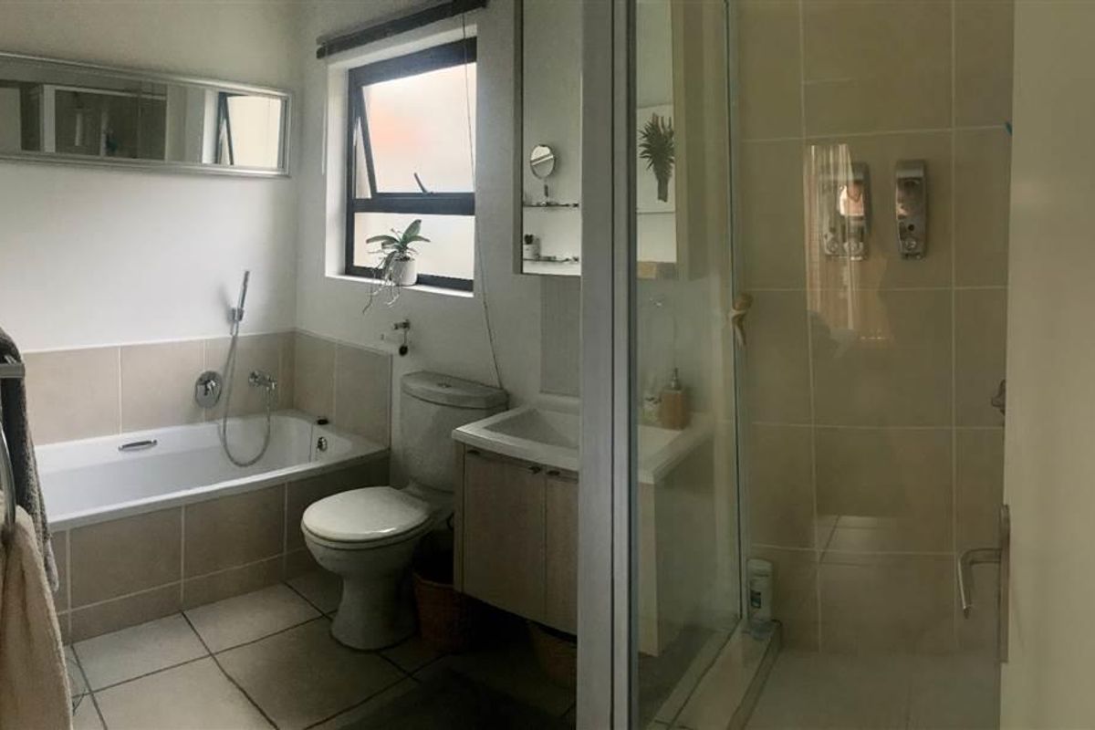 A functional bathroom featuring a built-in bathtub, separate shower enclosure, vanity cabinet, and neutral ceramic tiling throughout.