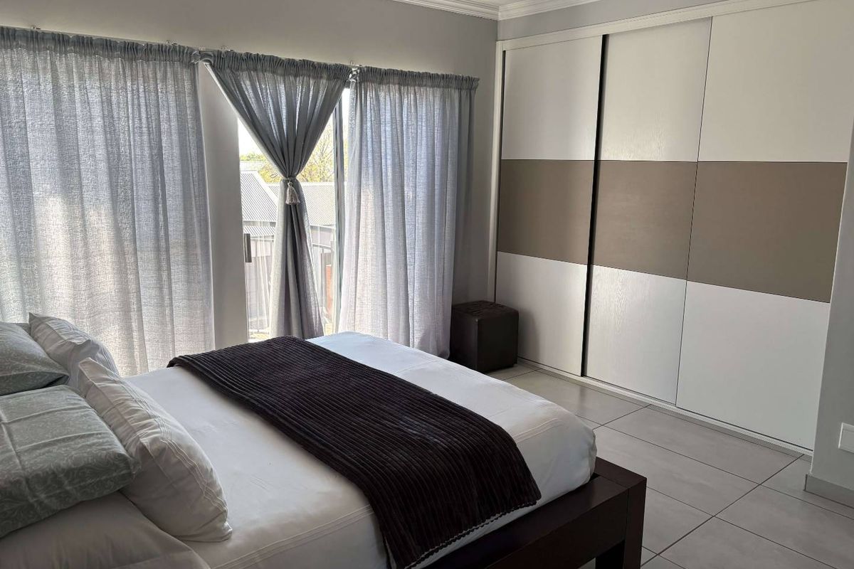 A well-maintained bedroom featuring large format floor tiles, a modern built-in sliding wardrobe, and a sliding glass door providing natural light.