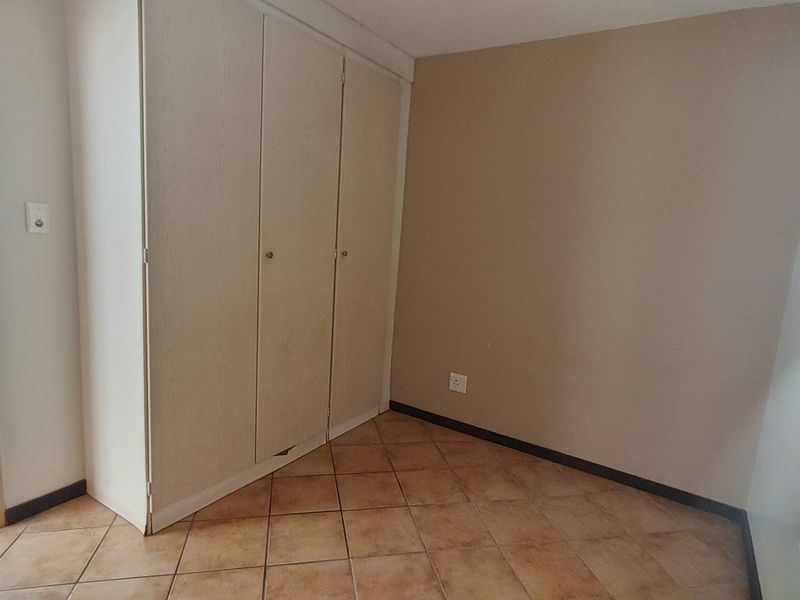 An empty bedroom featuring tiled flooring and a built-in wardrobe with some visible wear to the base.
