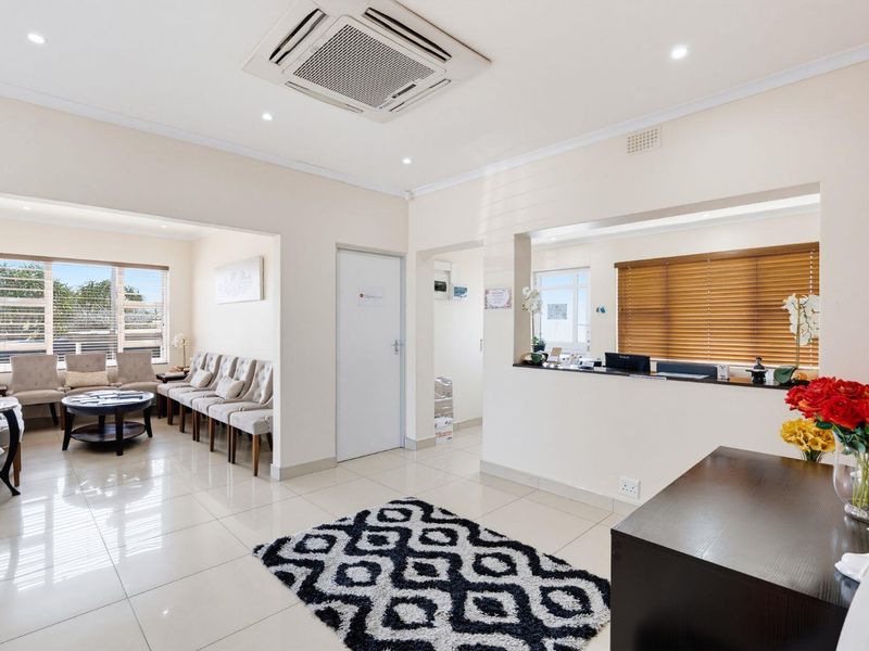 A bright and professional office reception area featuring tiled flooring, recessed lighting, a built-in reception counter, and a comfortable waiting area.