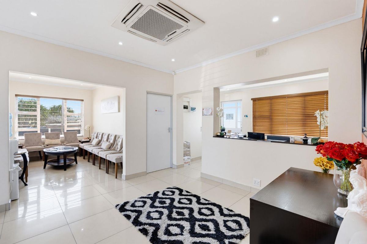 A bright and professional office reception area featuring tiled flooring, recessed lighting, a built-in reception counter, and a comfortable waiting area.