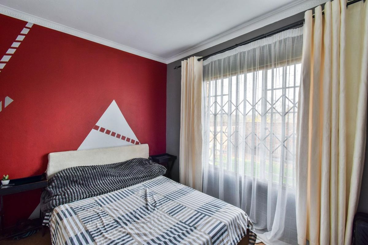 A bedroom featuring a large window with security bars, crown molding, and a bold red accent wall.