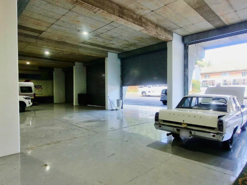 Spacious industrial garage featuring high concrete ceilings, polished concrete flooring, and multiple large roller shutter doors for easy vehicle access.