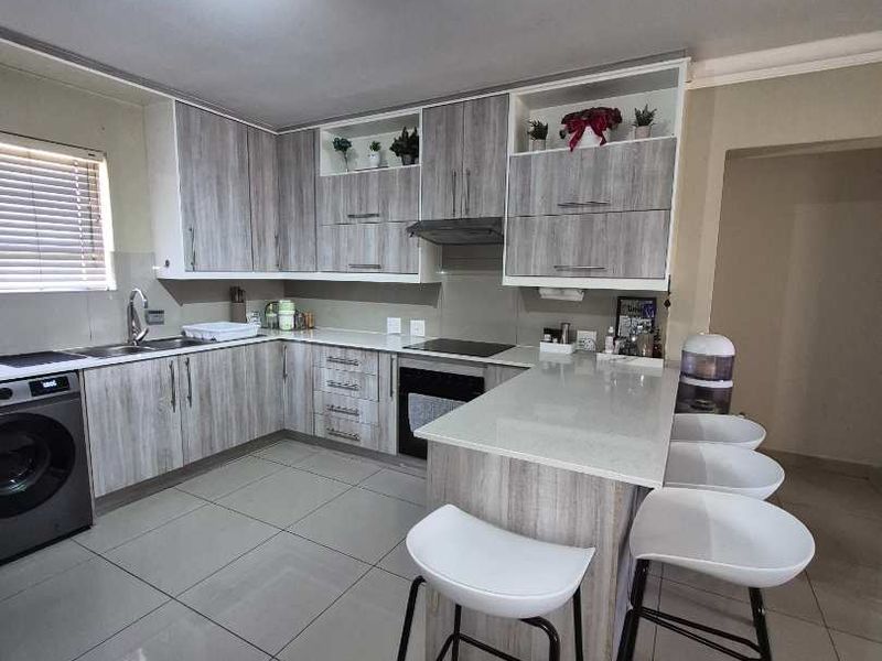 Modern kitchen featuring light wood-grain cabinetry, stone countertops, a breakfast bar, and integrated appliances with sleek tiled flooring.