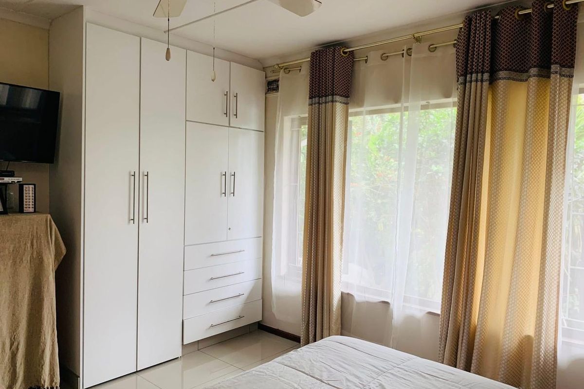 A well-maintained bedroom featuring built-in cupboards, tiled flooring, and a ceiling fan, offering a clean and functional living space.