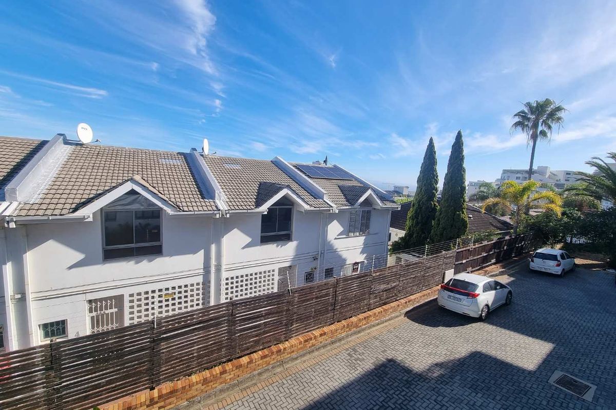 Rear exterior view of the apartment complex featuring a paved driveway, timber fencing, and roof-mounted solar panels under a clear blue sky.