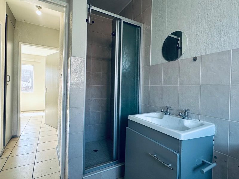 A functional bathroom featuring a shower enclosure, vanity cabinet with basin, and tiled finishes, presenting a clean but dated aesthetic.