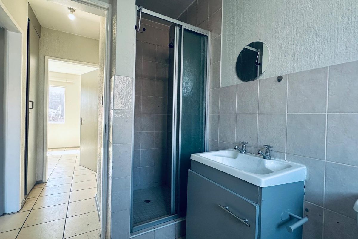 A functional bathroom featuring a shower enclosure, vanity cabinet with basin, and tiled finishes, presenting a clean but dated aesthetic.