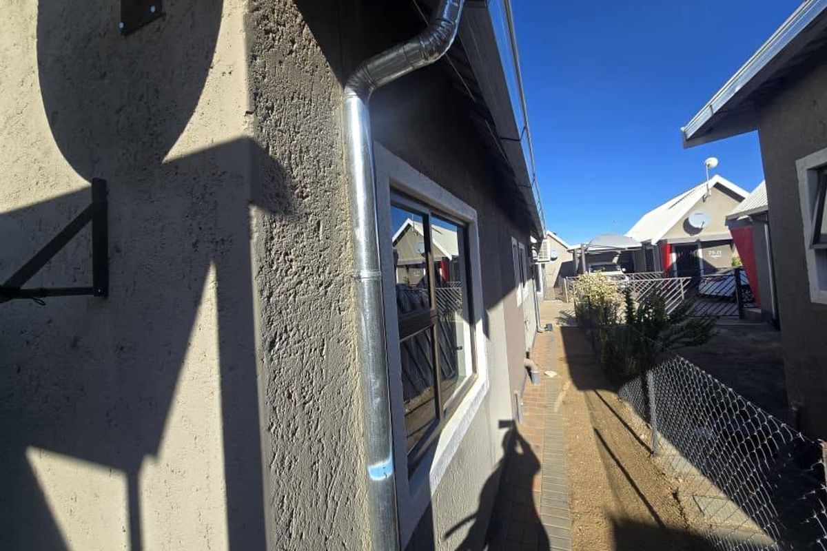 Side exterior view of the townhouse showing the building facade, metal downpipe, and paved walkway along the perimeter.