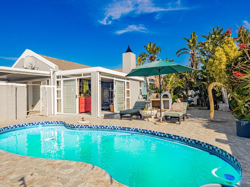 A well-maintained outdoor pool area featuring a tiled deck, built-in braai, and seamless access to the home through sliding glass doors.