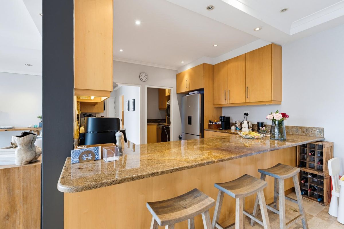 A functional kitchen featuring warm wooden cabinetry, granite countertops, and a breakfast bar, with an adjacent scullery area visible in the background.