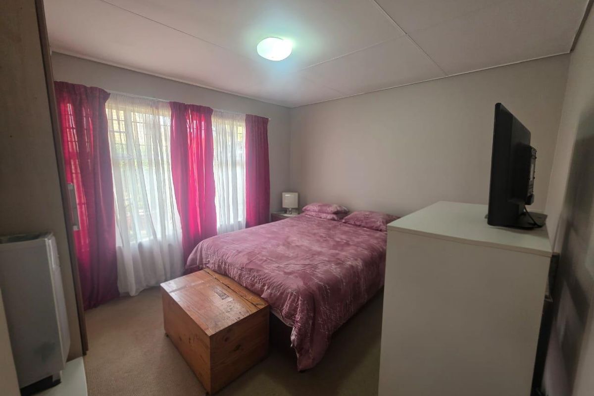 A functional bedroom featuring neutral wall finishes, carpeted flooring, and a window with curtain tracks.
