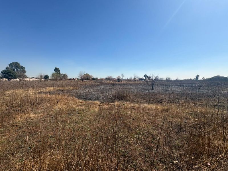 A view of a vacant residential plot featuring dry grass and signs of recent fire damage across the landscape.