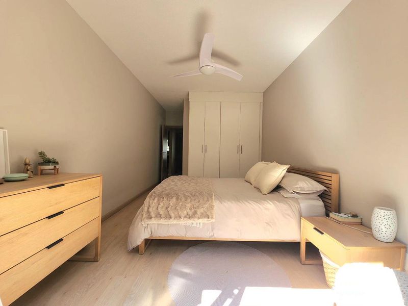 A well-maintained bedroom featuring light-toned laminate flooring, a modern ceiling fan, and ample built-in wardrobe storage.