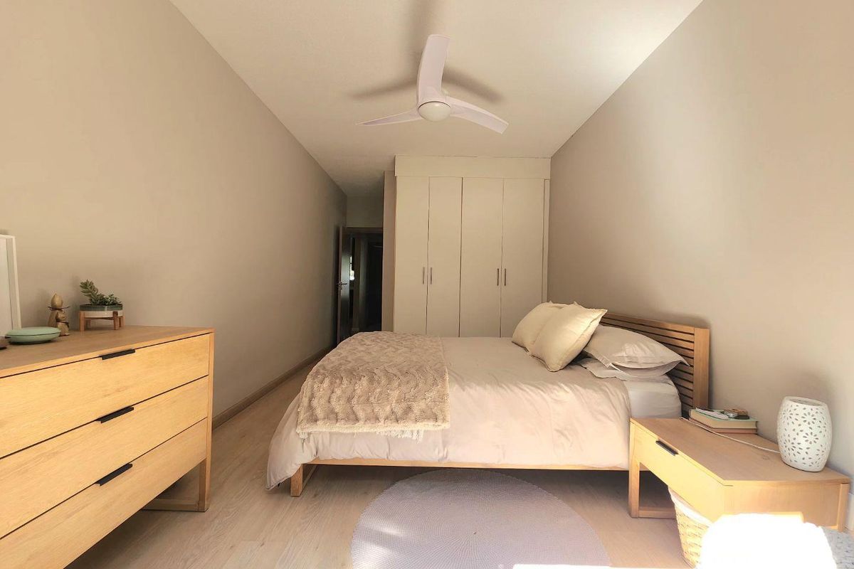 A well-maintained bedroom featuring light-toned laminate flooring, a modern ceiling fan, and ample built-in wardrobe storage.