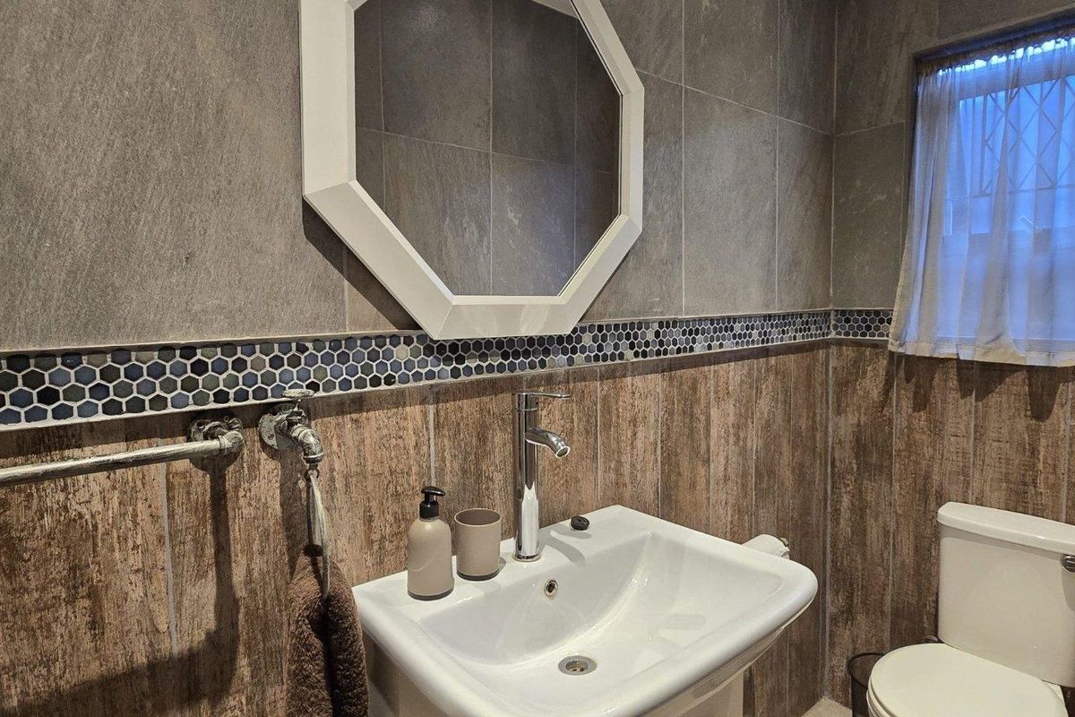A well-maintained bathroom featuring a pedestal basin with a modern mixer tap, a toilet, and decorative tiled walls with a mosaic accent border.