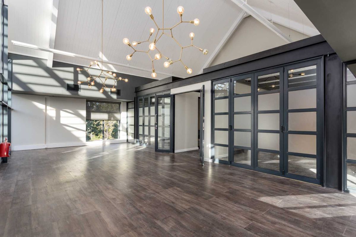 Spacious, modern office area featuring vaulted ceilings with exposed rafters, timber laminate flooring, and stylish black-framed glass partitions for a professional, open-plan feel.