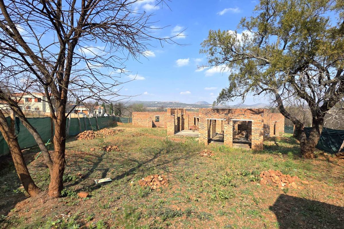 A view of a residential property under construction, featuring exposed brick walls and an unfinished structure on a large, undeveloped plot of land.