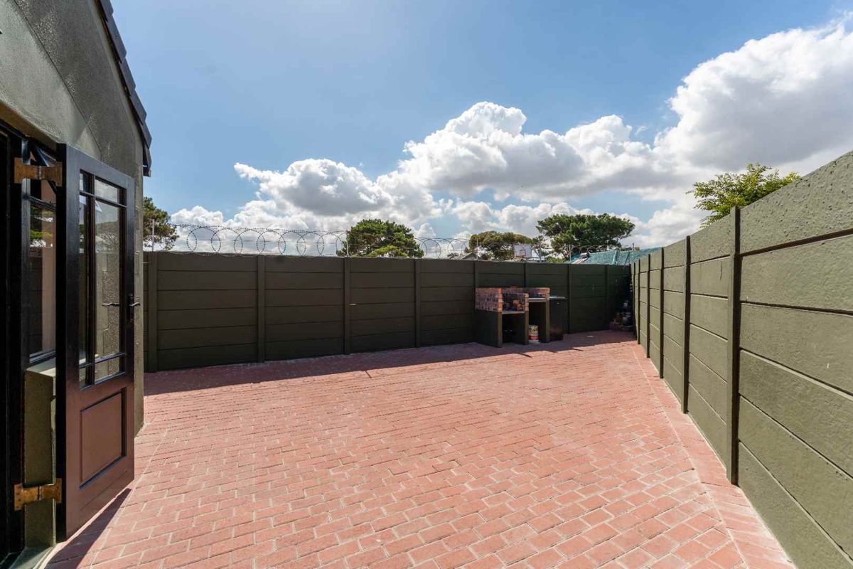 A private rear courtyard featuring red brick paving, high perimeter walls with security fencing, and a built-in brick braai area.