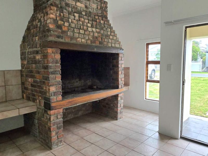 Covered patio area featuring a large built-in brick fireplace, tiled flooring, and direct access to the garden through sliding glass doors.