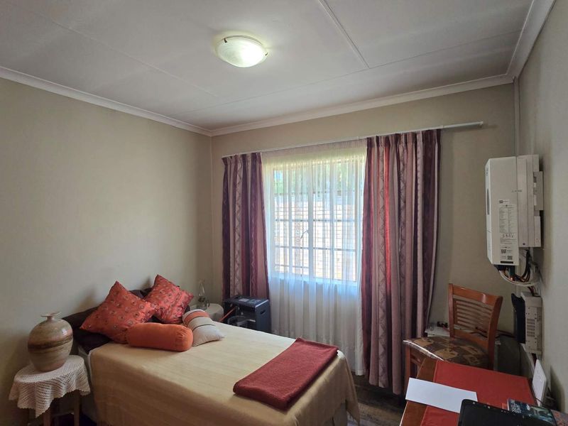 A functional bedroom featuring a window with security bars and a wall-mounted electric water heater unit.