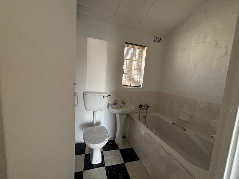 A functional bathroom featuring a pedestal basin, toilet, and bathtub with tiled splashbacks and a classic black and white checkered floor.