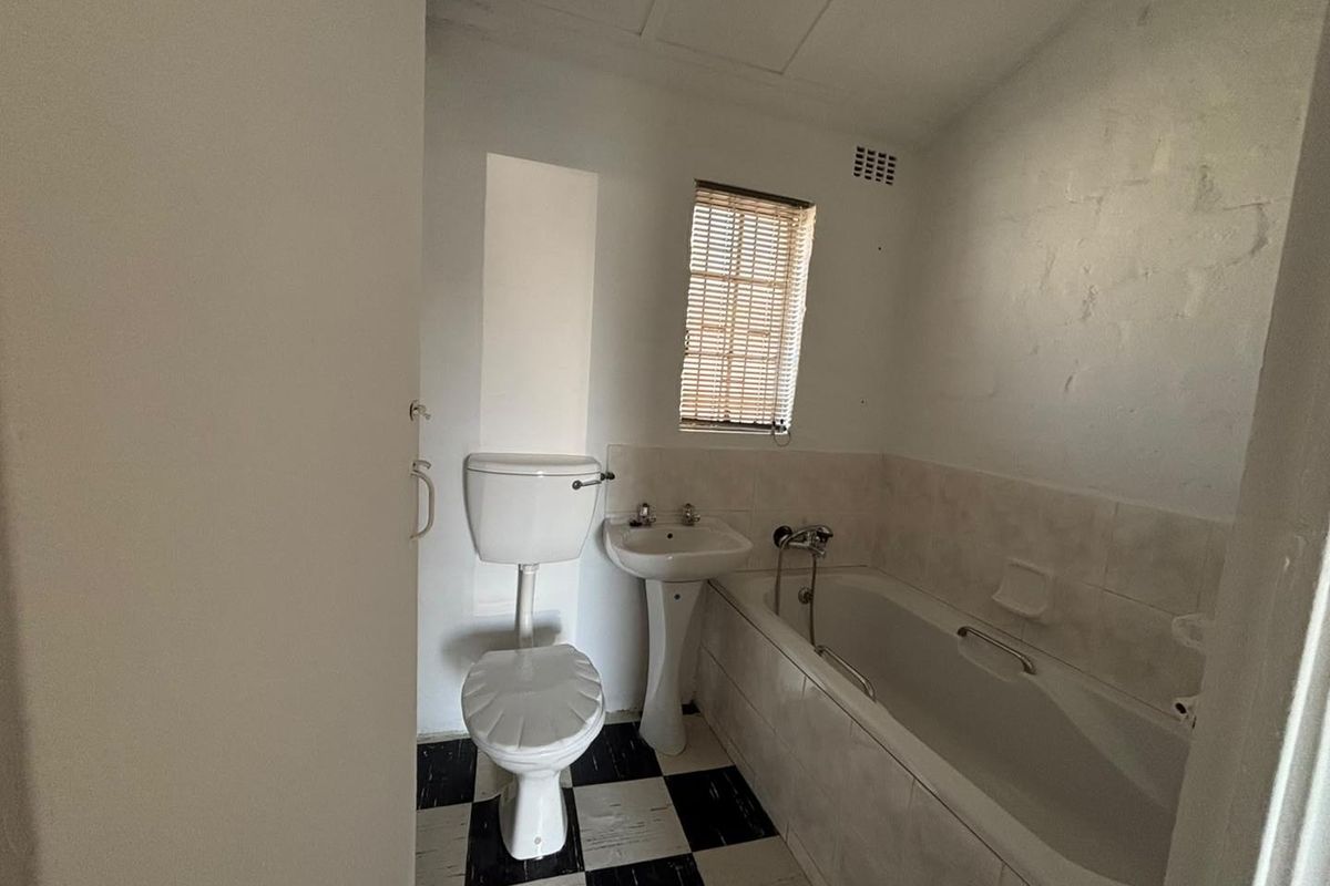 A functional bathroom featuring a pedestal basin, toilet, and bathtub with tiled splashbacks and a classic black and white checkered floor.