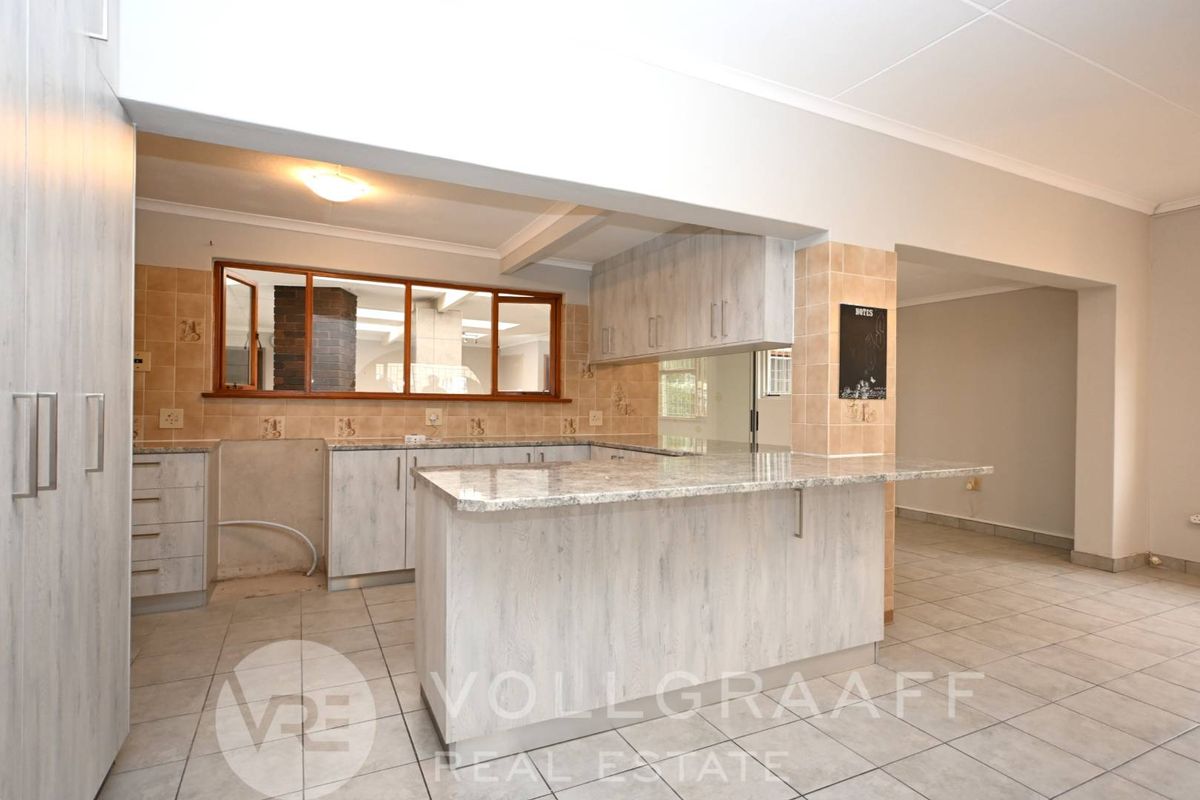 A functional kitchen featuring light wood-grain cabinetry, stone-look countertops, a breakfast bar, and tiled flooring, with an open-plan layout connecting to adjacent living areas.