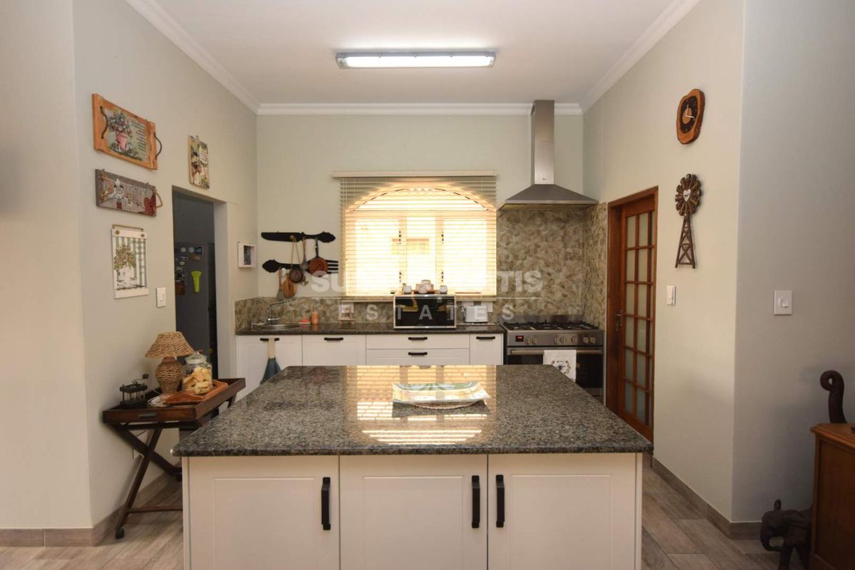 A functional kitchen featuring a central island with granite countertops, built-in cabinetry, a stainless steel extractor fan, and a gas stove.