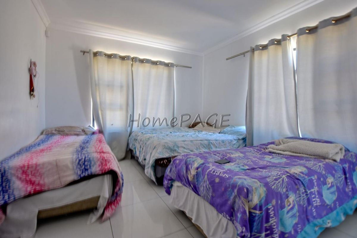 A spacious bedroom featuring tiled flooring, neutral walls, and large windows with installed curtain rods.