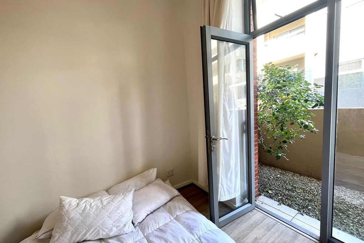 Bedroom featuring laminate flooring and a large aluminium framed glass door providing direct access to a private outdoor area.