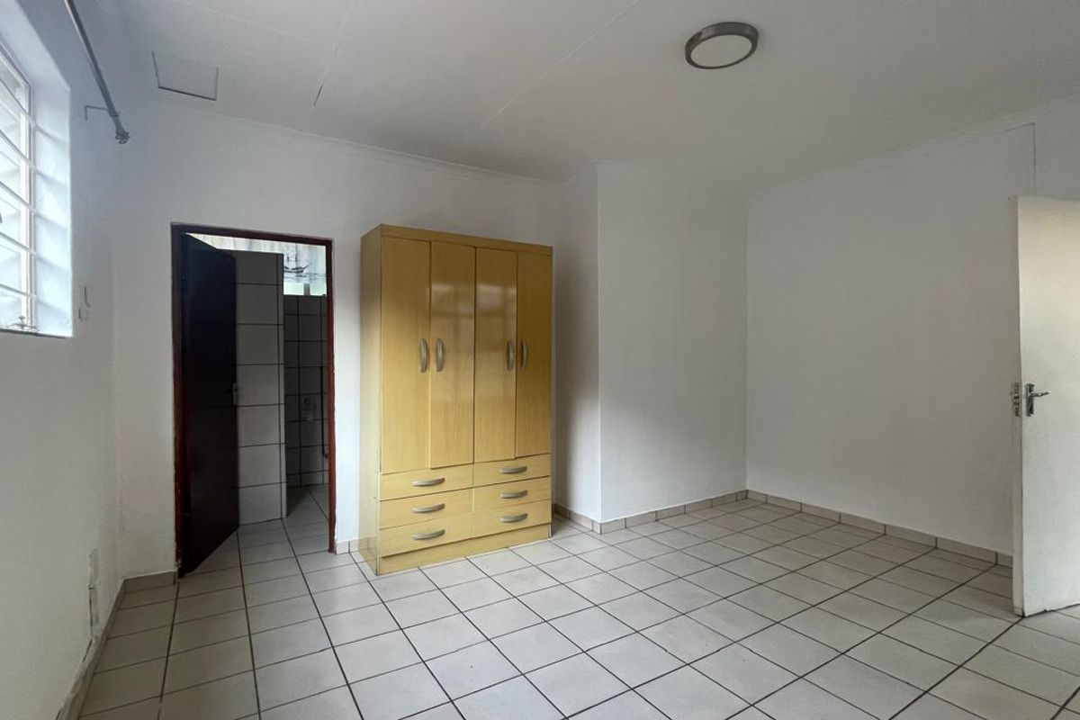 A functional bedroom featuring tiled flooring, a built-in wardrobe, and a glass block window, providing a neutral space ready for personalization.