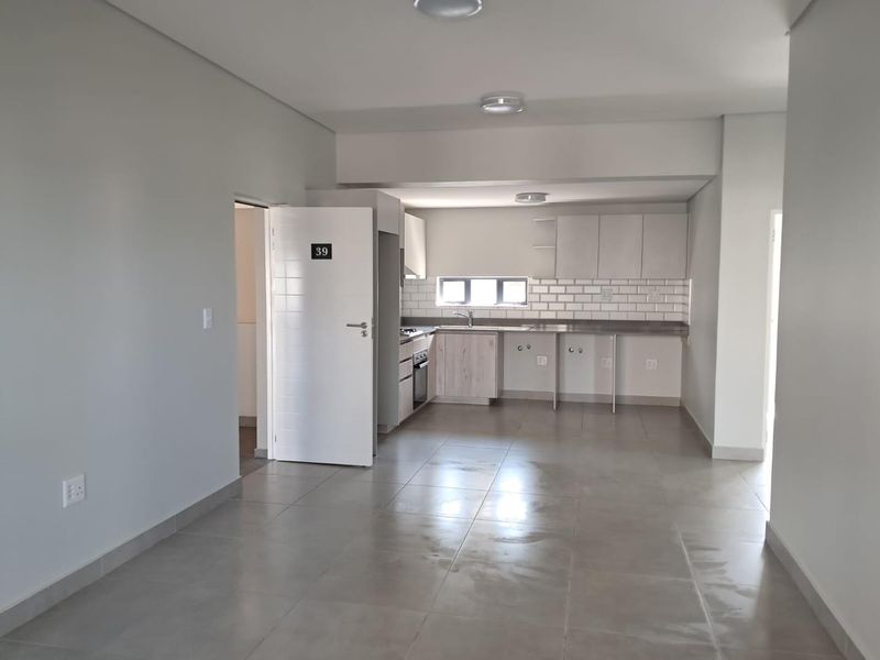 Open plan living area featuring a modern kitchen with built-in cabinetry, subway tile backsplash, and neutral ceramic floor tiles throughout.