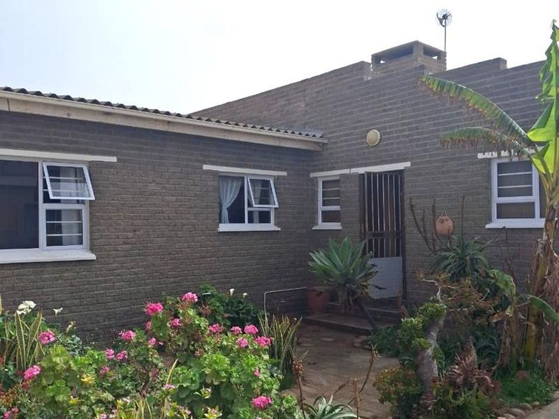 Rear view of the house featuring a brick facade, paved walkway, and established garden beds.