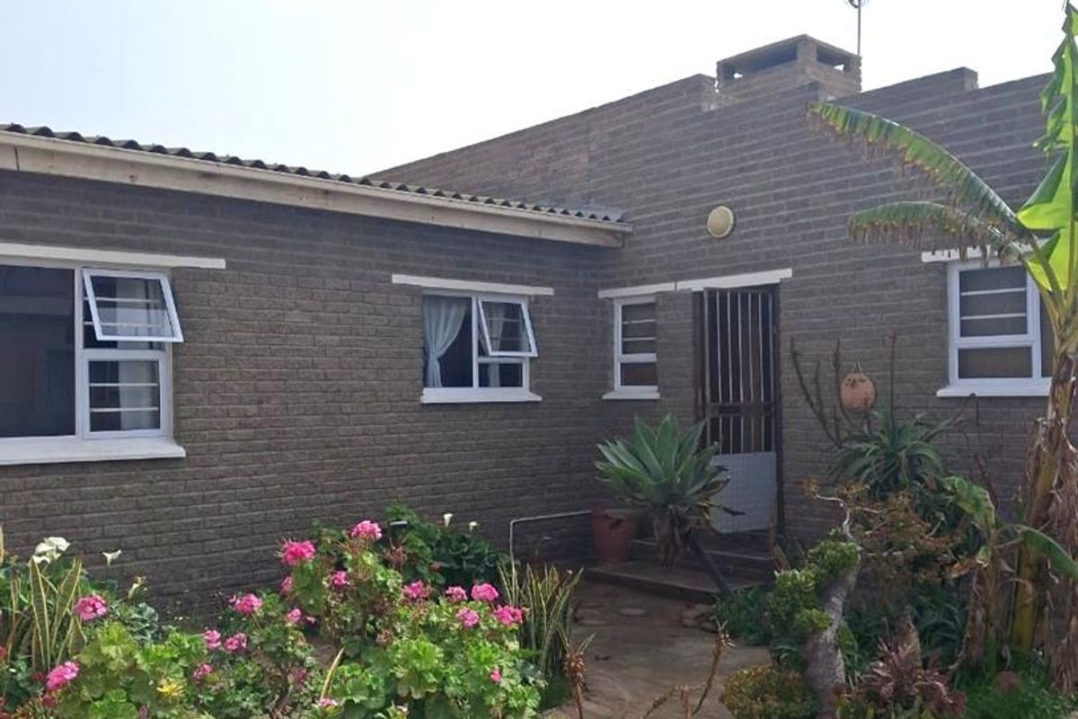 Rear view of the house featuring a brick facade, paved walkway, and established garden beds.