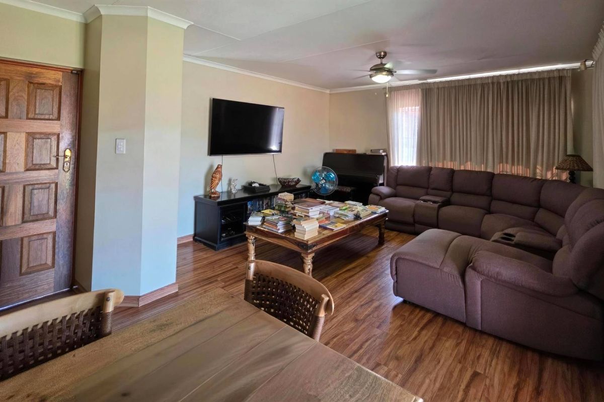 Spacious living room featuring warm laminate flooring, a ceiling fan, and classic cove cornicing, providing a comfortable and functional family space.