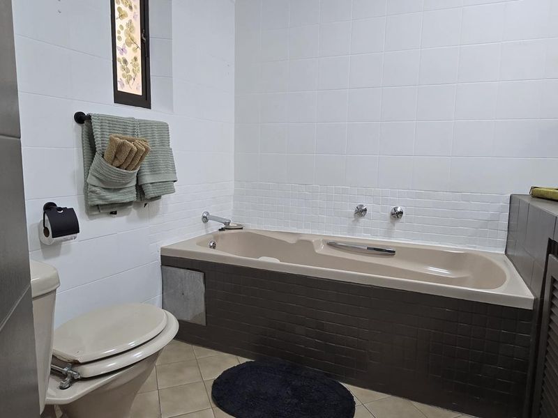A functional bathroom featuring a built-in bathtub, vanity cabinet with basin, and tiled finishes throughout.