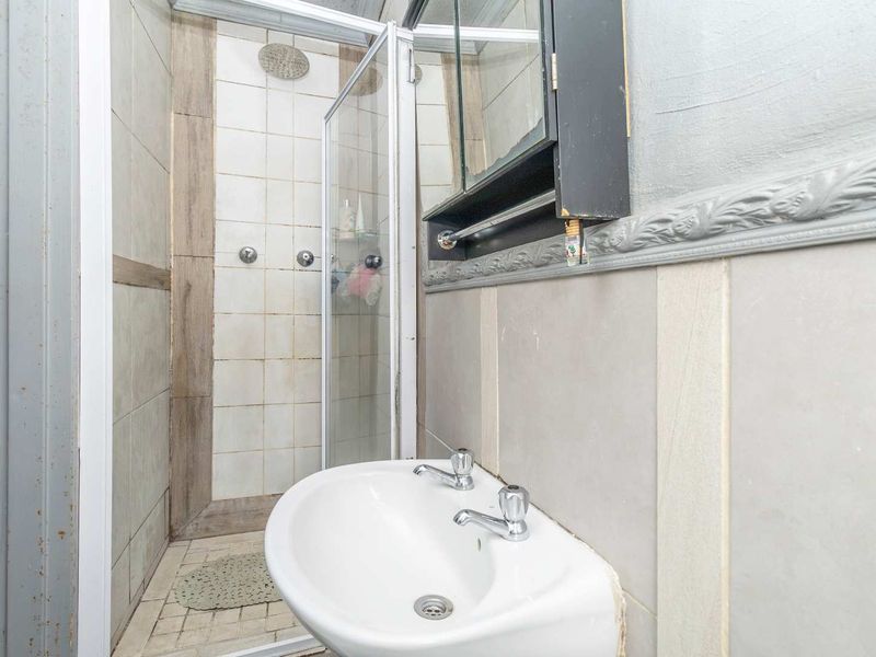 Compact bathroom featuring a shower enclosure, wall-mounted basin, and medicine cabinet, showing signs of wear and dated finishes.