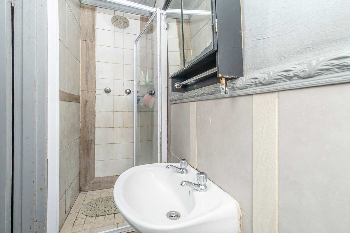 Compact bathroom featuring a shower enclosure, wall-mounted basin, and medicine cabinet, showing signs of wear and dated finishes.