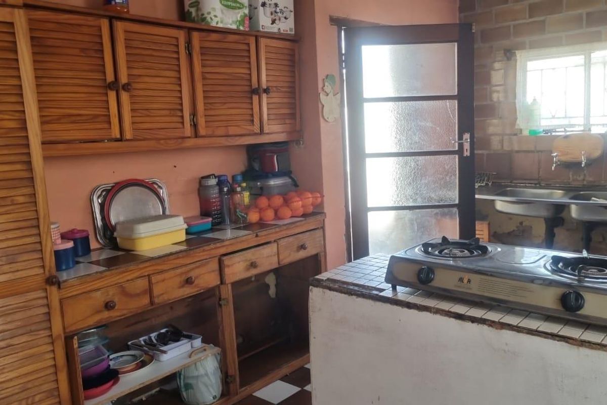 A dated kitchen featuring wooden cabinetry, a tiled island with a gas cooktop, and a double basin sink with exposed brick wall detailing.