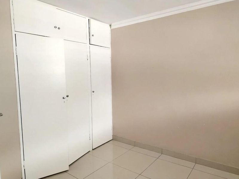 An empty bedroom featuring neutral wall paint, tiled flooring, and white built-in cupboards with overhead storage.