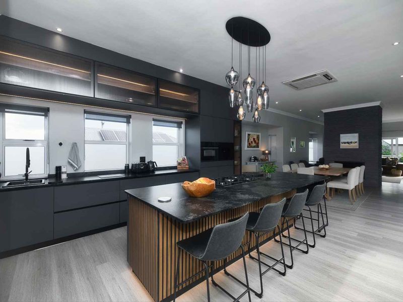 Modern open-plan kitchen featuring a large central island, sleek dark cabinetry, integrated appliances, and high-end finishes, seamlessly flowing into the dining and living areas.